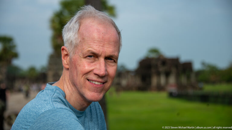 Close portrait of a gray-haired man with temple lawn blurred behind at Angkor Wat.
