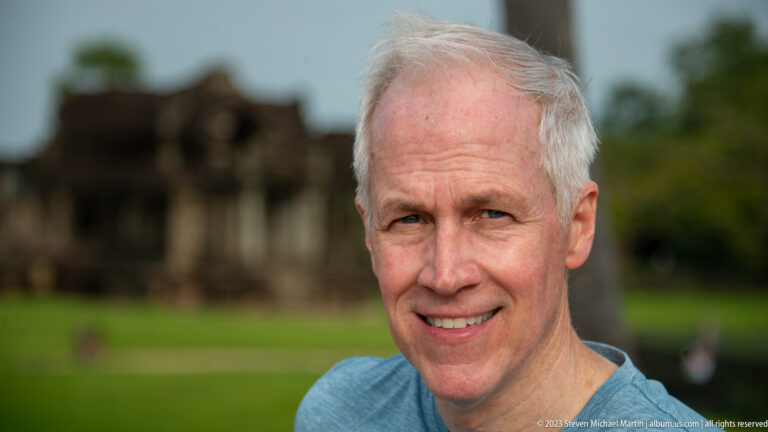 Second close smiling portrait of the same gray-haired man at Angkor Wat.