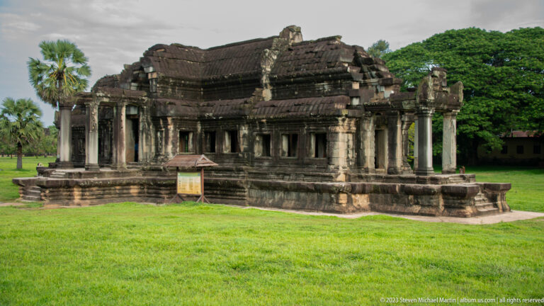 Long colonnaded gallery viewed across bright green grass at Angkor Wat.