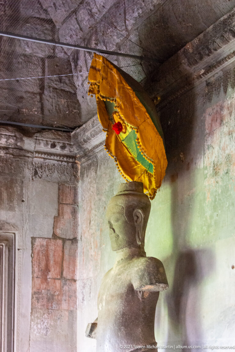 Golden and red ceremonial parasol or banner hanging beside a stone column at Angkor Wat.