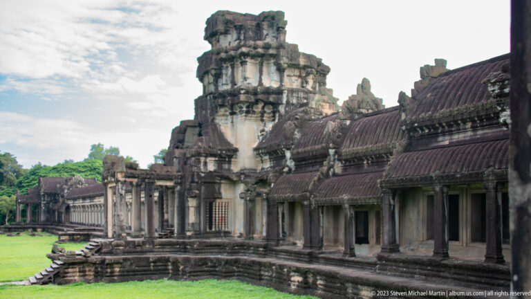 Oblique gallery and tower reflected along a narrow water channel at Angkor Wat.