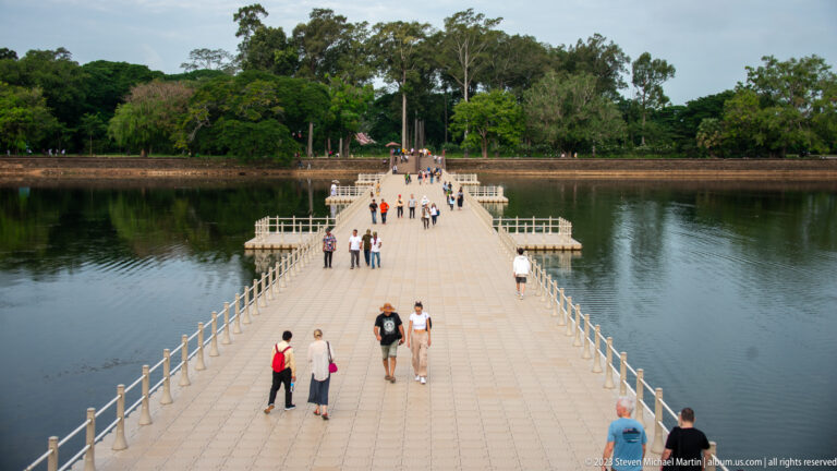 Long stone causeway crossing the moat with visitors walking toward the entrance at Angkor Wat.