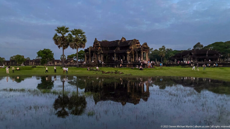 Low pavilion and palms reflected in a pond under blue evening sky at Angkor Wat.
