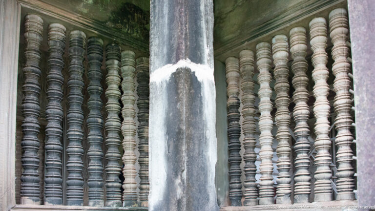 Close view of repeating turned stone window balusters divided by a dark central pillar at Angkor Wat.