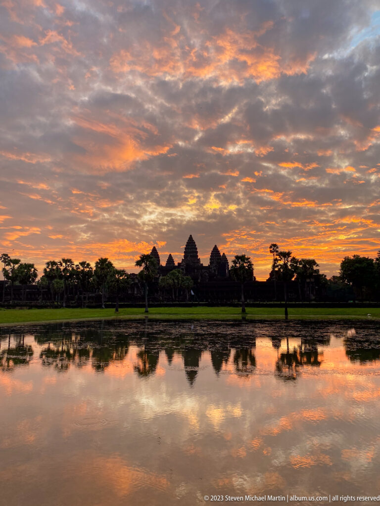 Very wide dark tower silhouette beneath a richly orange clouded sky and reflection at Angkor Wat.