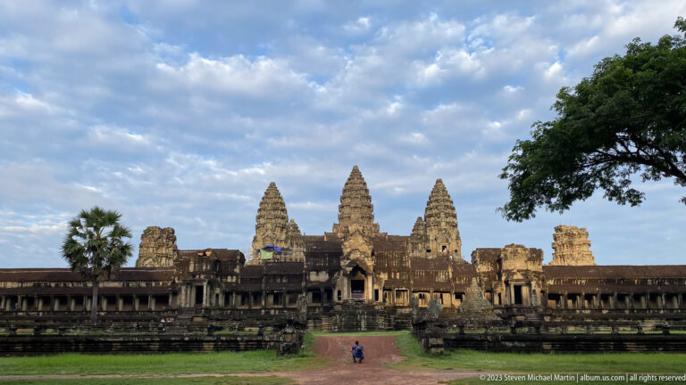 Wide daylight frontal view of three towers with two small visitors on the path at Angkor Wat.