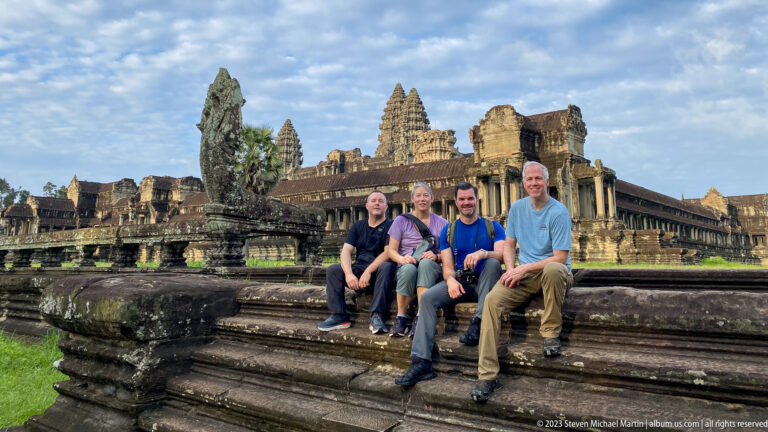 Four visitors seated together on stone steps with towers behind at Angkor Wat.
