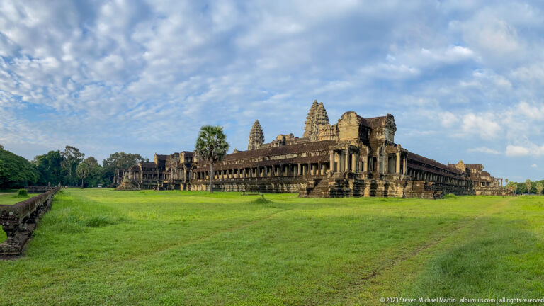 Very wide side elevation of the long gallery and towers across a large green lawn at Angkor Wat.