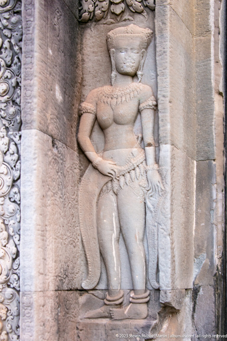 Close cropped standing devata with jewelry, patterned skirt, and one hand at the waist at Angkor Wat.