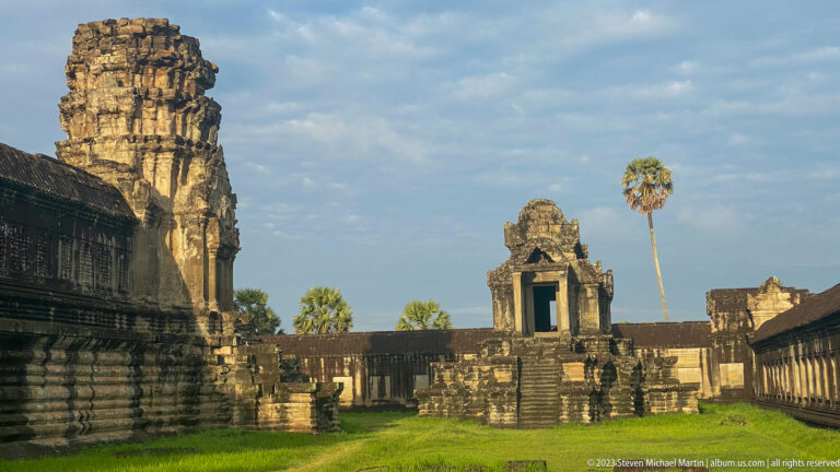 Distant small shrine framed between a large tower edge and open lawn at Angkor Wat.