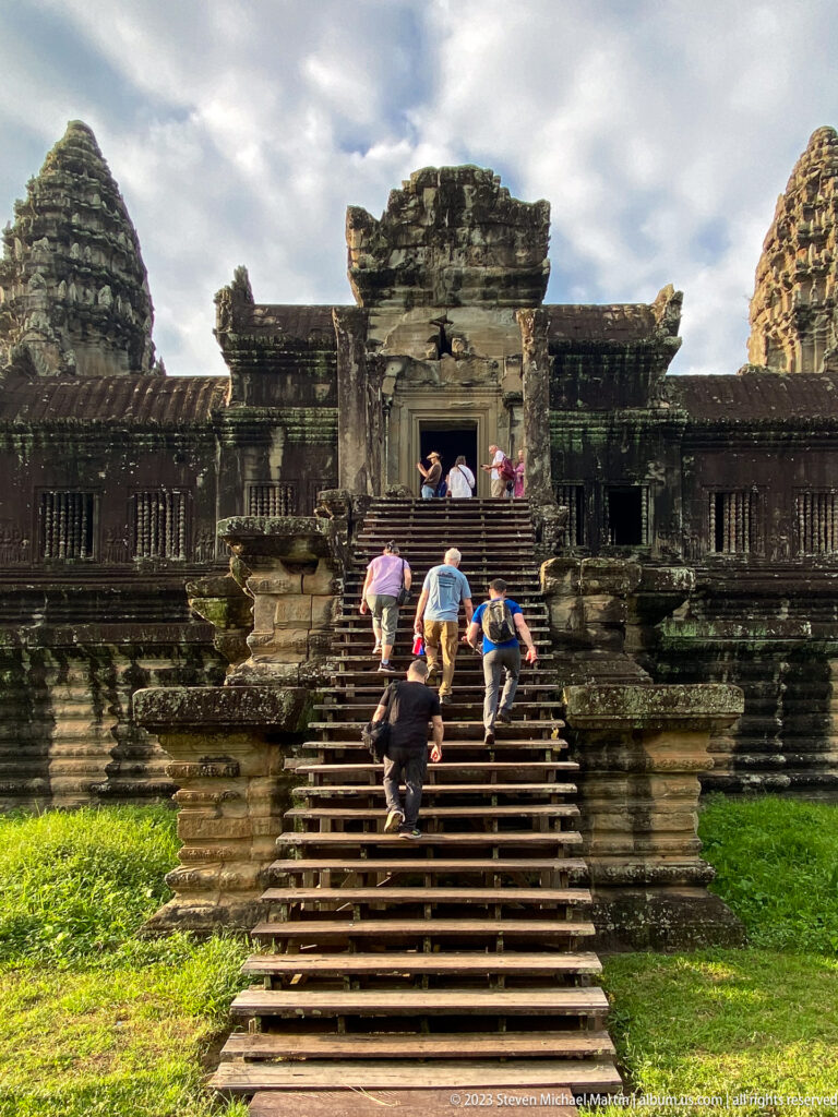 Visitors climbing broad stone steps into a central doorway at Angkor Wat.