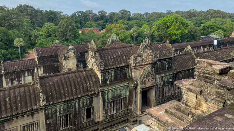 Elevated view over weathered gallery roofs toward the surrounding green landscape at Angkor Wat.