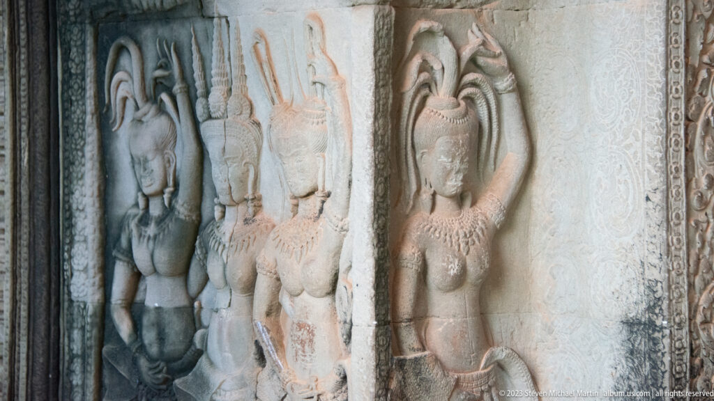 Three weathered female figures or devatas carved in a narrow wall panel at Angkor Wat.