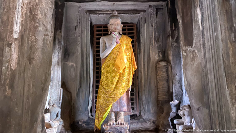 Standing Buddha statue draped in gold cloth inside a dark doorway at Angkor Wat.