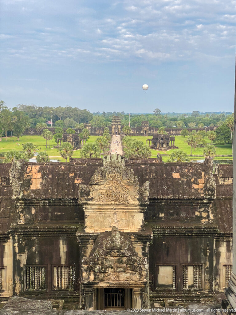 High view over a central tower roof toward the long causeway and surrounding forest at Angkor Wat.