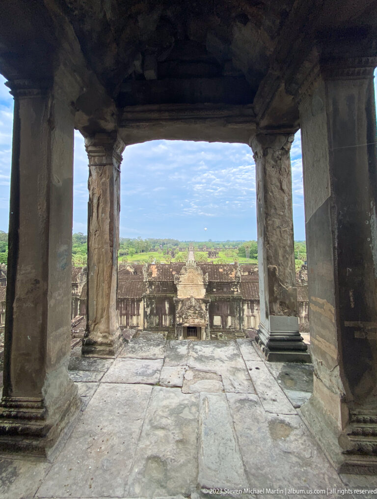 View through a stone window opening over roofs, courtyards, and distant landscape at Angkor Wat.