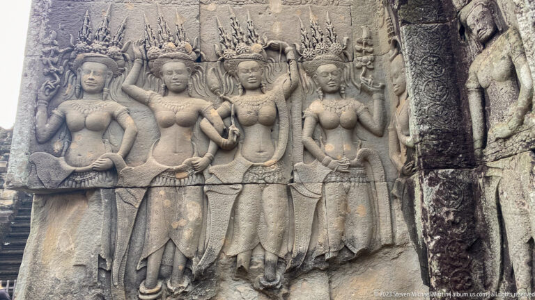 Three standing devatas carved together in a rectangular panel at Angkor Wat.