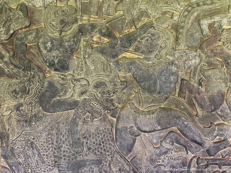Dark weathered relief of a large animal or mounted figure amid combat at Angkor Wat.
