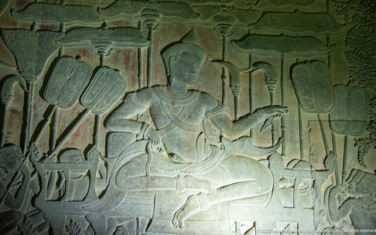 Bas-relief scene with a large seated or reclining figure and attendants in shallow sandstone carving at Angkor Wat.