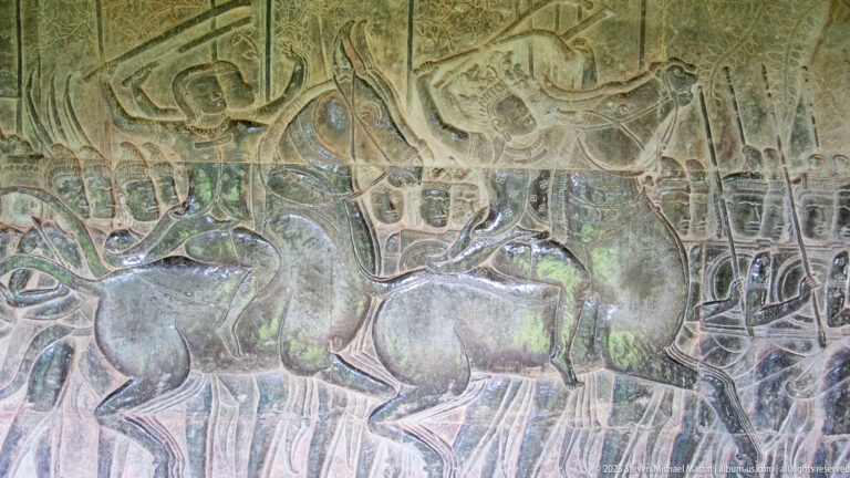 Dynamic relief of large animals and human figures in a crowded battle or procession scene at Angkor Wat.