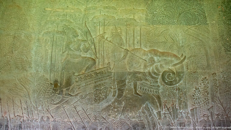 Faint relief with a long vessel, standing figures, and a large curling circular motif at Angkor Wat.