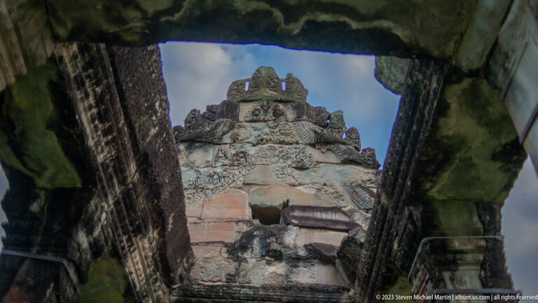 Upward view through a dark stone opening toward the weathered upper profile of a tower at Angkor Wat.