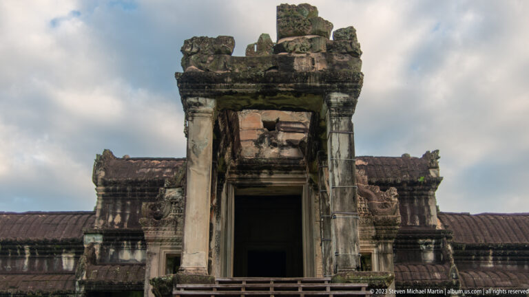 Frontal weathered doorway with dark interior beneath a broken pediment at Angkor Wat.