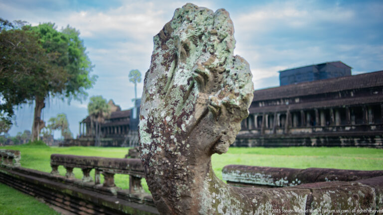 Close eroded stone guardian head with the gallery and lawn behind at Angkor Wat.