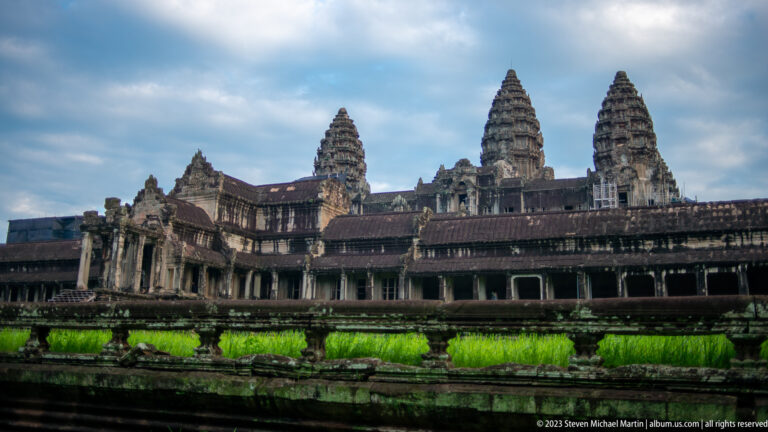 Wide exterior view of Angkor Wat’s galleries and three towers under blue sky at Angkor Wat.