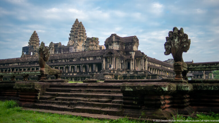 Similar oblique façade view with prominent stone guardian figure at the right edge at Angkor Wat.