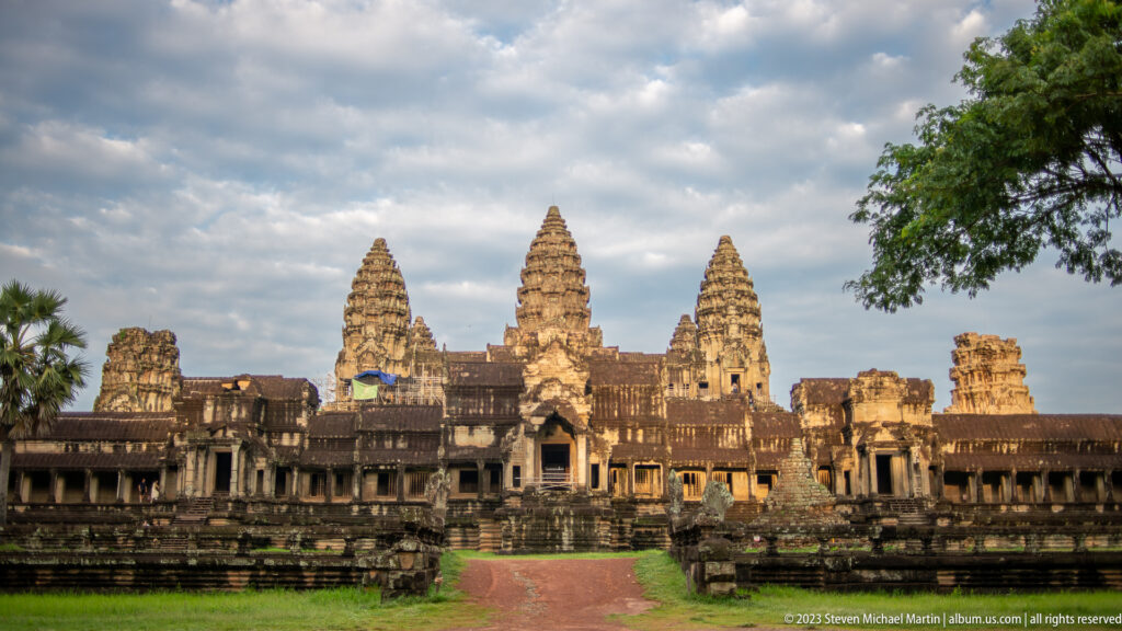 Symmetrical frontal view of Angkor Wat’s three principal towers across a reddish central path at Angkor Wat.
