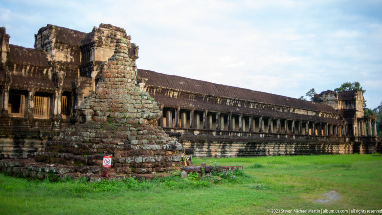 Side gallery corner with long colonnade, lawn, and weathered masonry at Angkor Wat.