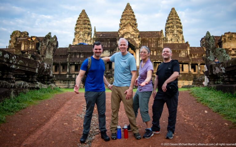 Four visitors standing on the reddish approach with Angkor Wat behind at Angkor Wat.