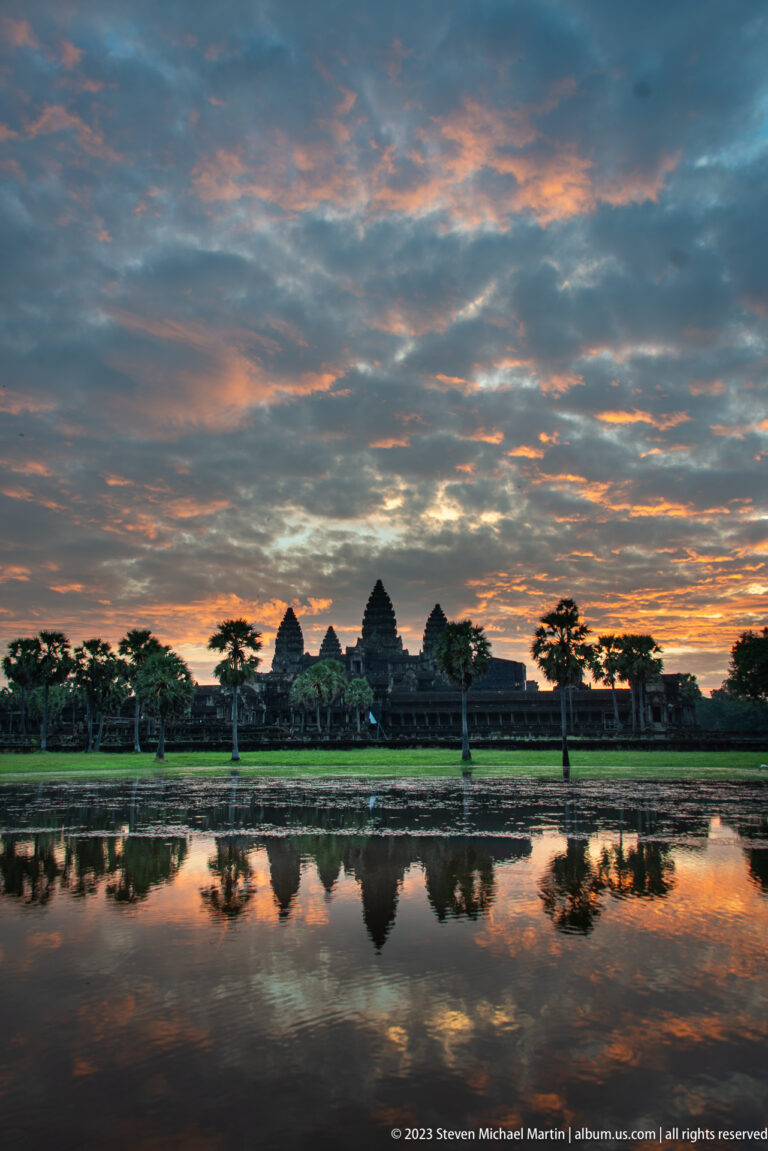 Low panoramic dawn view with small Angkor Wat towers below a richly textured orange-blue sky at Angkor Wat.