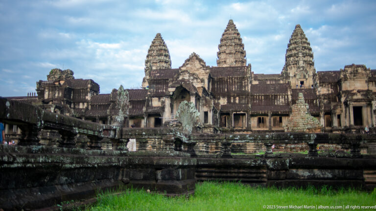 Wide architectural view of towers and western galleries across a dark terrace at Angkor Wat.