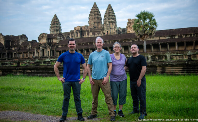 Four visitors posing on green grass in front of the long gallery and towers at Angkor Wat.