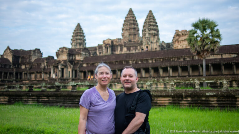Two visitors, a woman in purple and a man in black, posing before Angkor Wat at Angkor Wat.