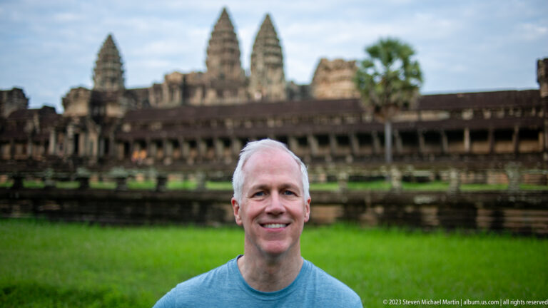 Close portrait of a smiling gray-haired man with Angkor Wat blurred behind at Angkor Wat.