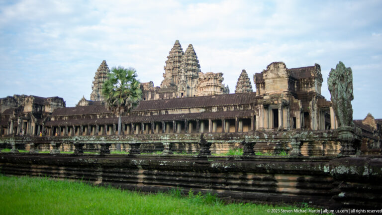 Wide side elevation of long gallery and towers under a blue sky at Angkor Wat.