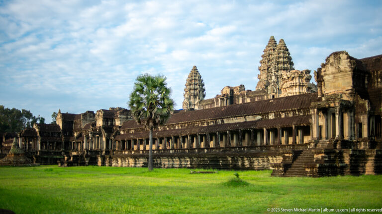 Long side gallery and towers viewed across a bright green lawn at Angkor Wat.