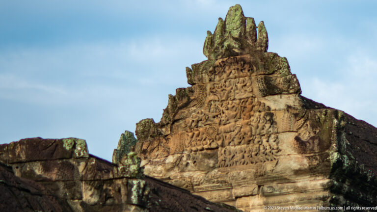 Weathered triangular pediment with a central seated figure above dense narrative carving at Angkor Wat.
