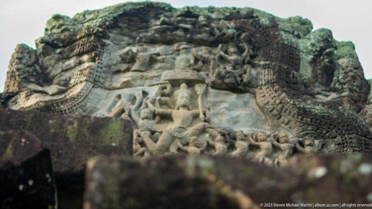 Close eroded pediment relief with a central figure and surrounding attendants at Angkor Wat.