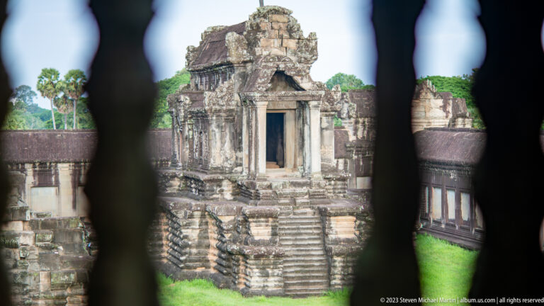 Distant shrine framed through dark out-of-focus stone balusters at Angkor Wat.
