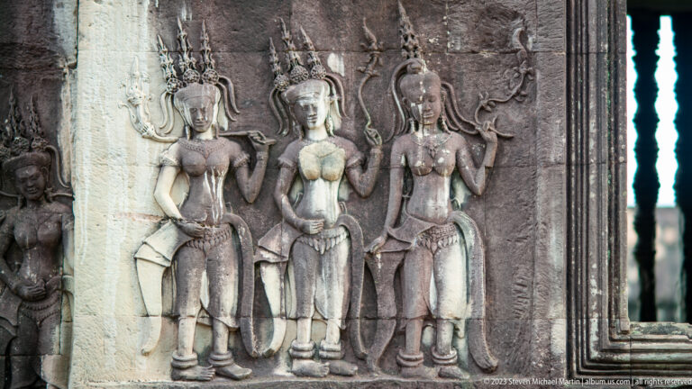 Three standing devatas with elaborate crowns and curling foliage at Angkor Wat.