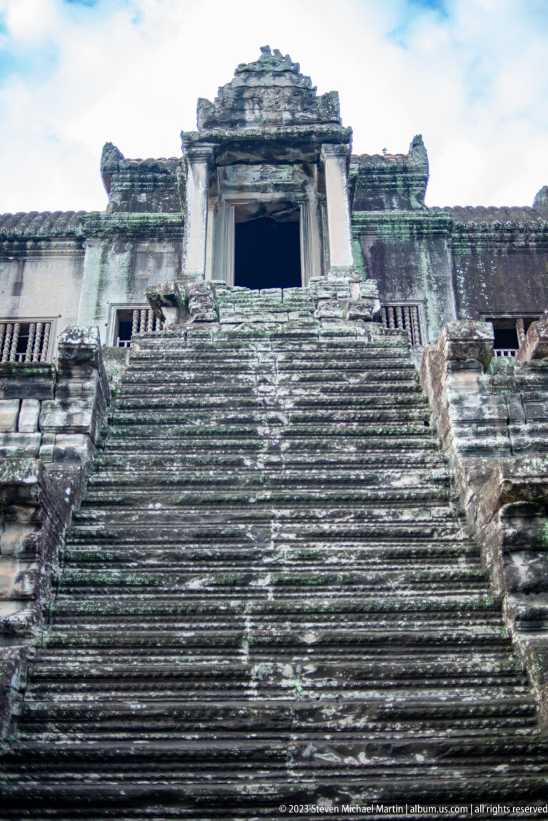 Very steep worn stone staircase rising to a dark upper doorway at Angkor Wat.