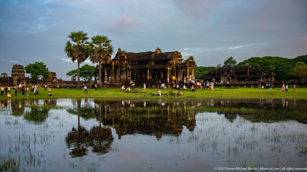 Long low pavilion and visitors reflected in a calm pool near the Angkor Wat approach at Angkor Wat.