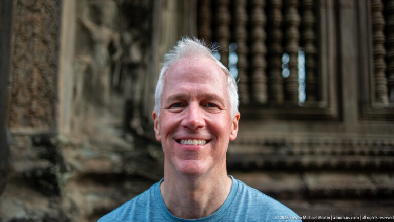 Close smiling portrait of a gray-haired visitor with balusters blurred behind at Angkor Wat.