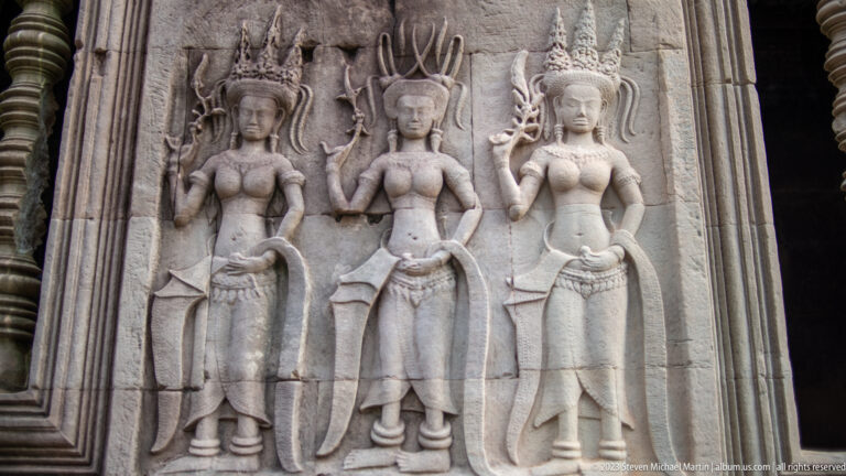 Three standing devatas with distinct headdresses and jewelry at Angkor Wat.