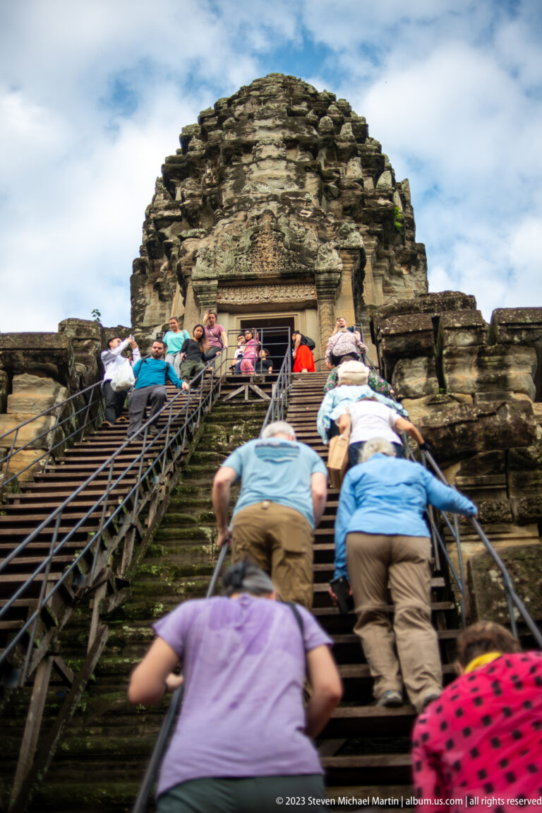 Visitors climbing a steep modern metal access stair into the upper sanctuary at Angkor Wat.