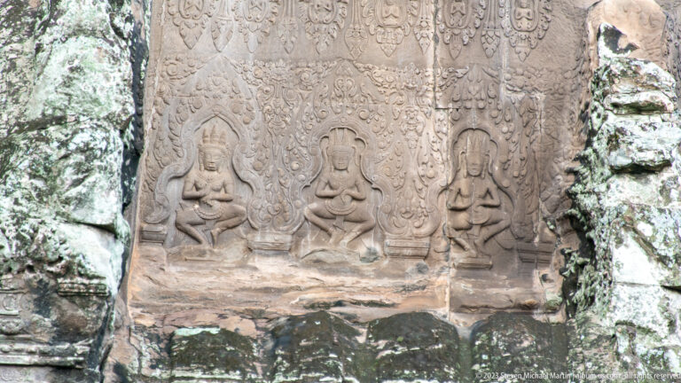 Three small seated sacred figures carved near the base of a panel at Angkor Wat.